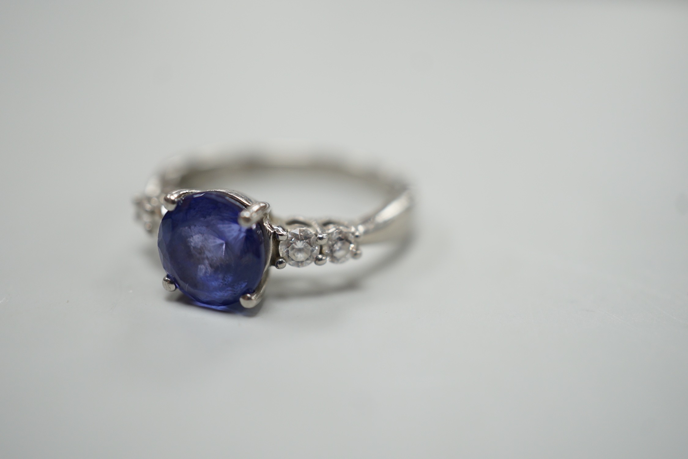 A modern Illiana platinum, single stone round cut tanzanite and four stone diamond set dress ring, size O, gross weight 5.7 grams.